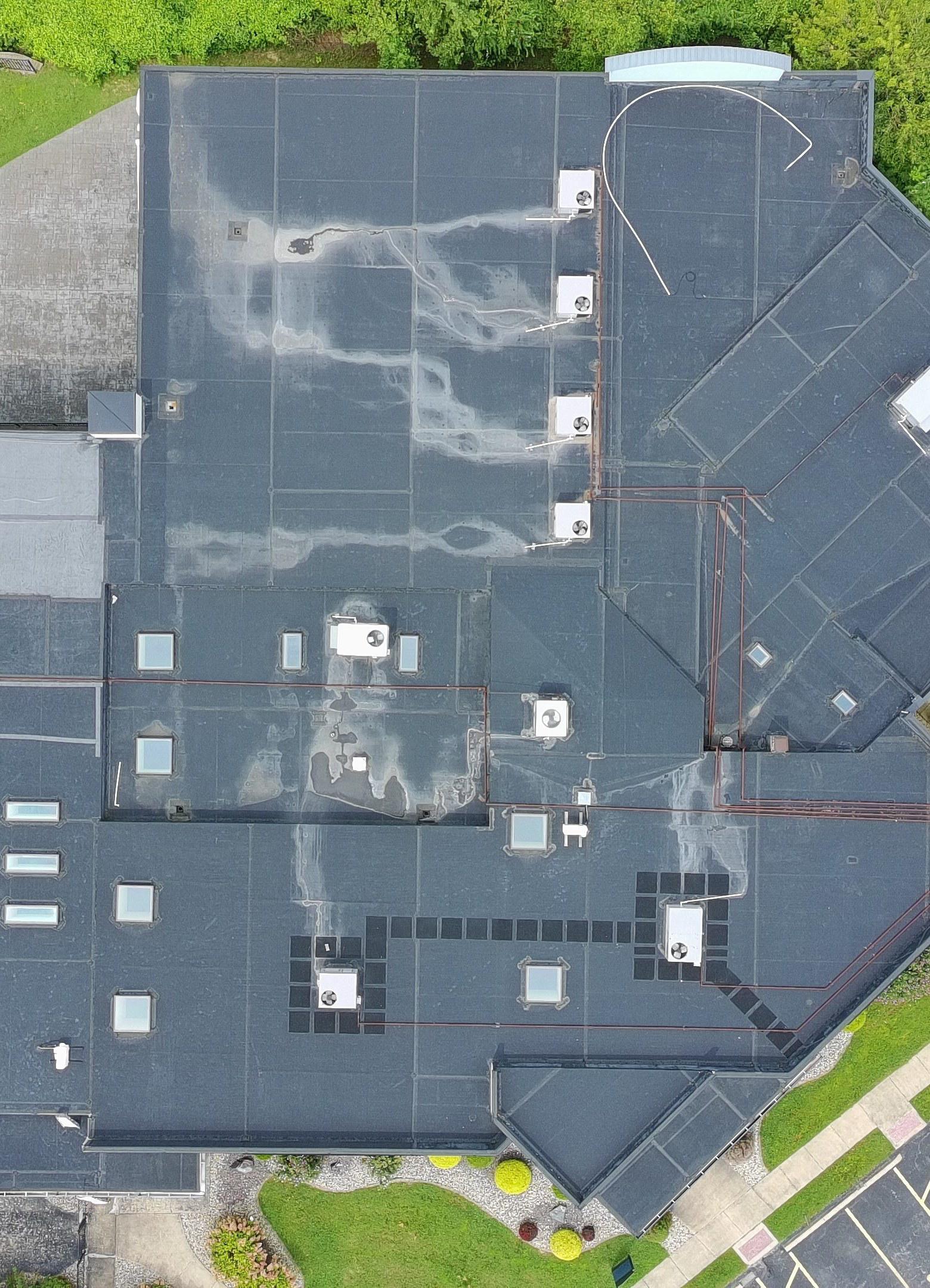 Aerial drone view of a large commercial building's flat roof showing storm damage and ponding across the membrane, captured during a claim inspection