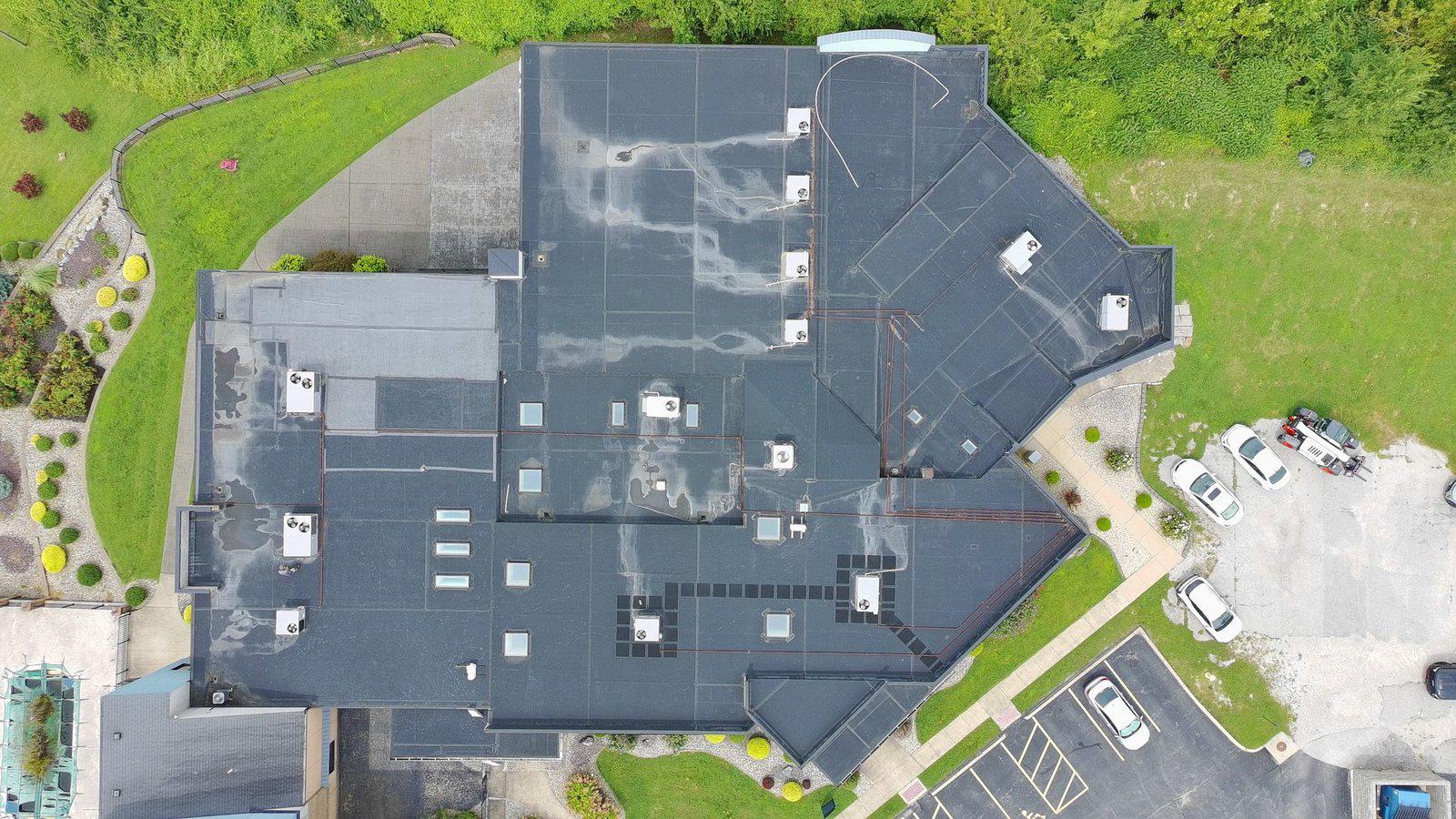 Aerial drone view of a large commercial building's flat roof showing storm damage and ponding across the membrane, captured during a claim inspection